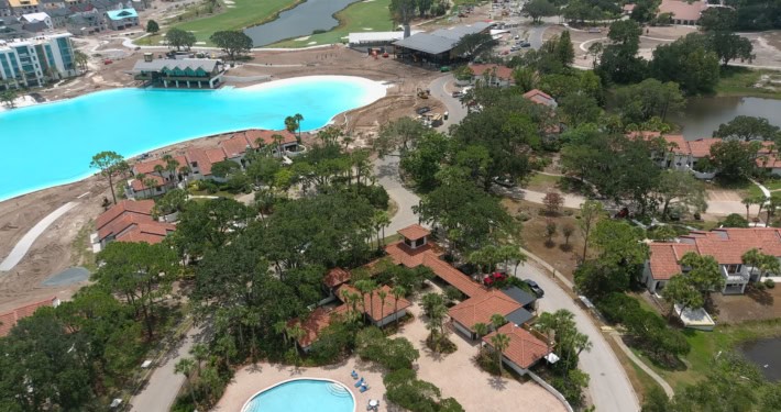 Modern resort pool area with water features, surrounding trees, and outdoor amenities.